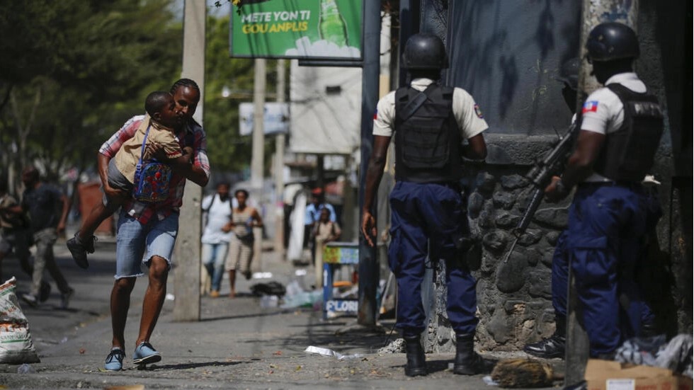  Un parent, portant son enfant après l'avoir récupéré à l'école, passe devant la police menant une opération contre les gangs dans le quartier de Bel-Air à Port-au-Prince, Haïti, le 3 mars 2023. (Image d'illustration) © Odelyn Joseph / AP 